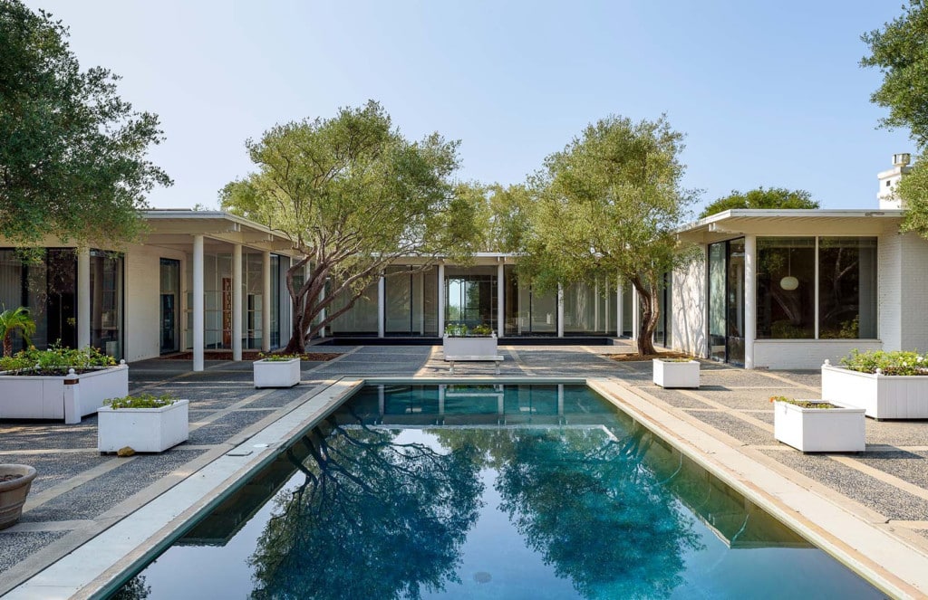 A stunning mid-century modern home designed by Lutah Maria Riggs, characterized by its sleek lines, minimalist design, and integration with nature. The house boasts floor-to-ceiling windows that invite abundant natural light into the spacious interior. In the backyard, a refreshing pool glistens under the sun, creating a tranquil and luxurious retreat.