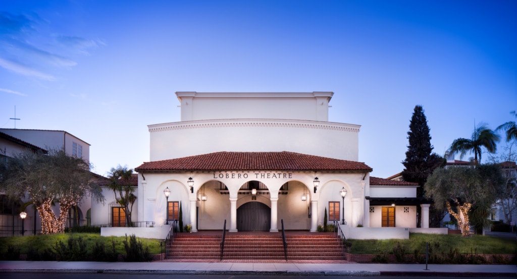 An enchanting view of the historic Lobero Theater in Santa Barbara at dusk, with warm golden lights illuminating the elegant facade against a backdrop of a vibrant sky.